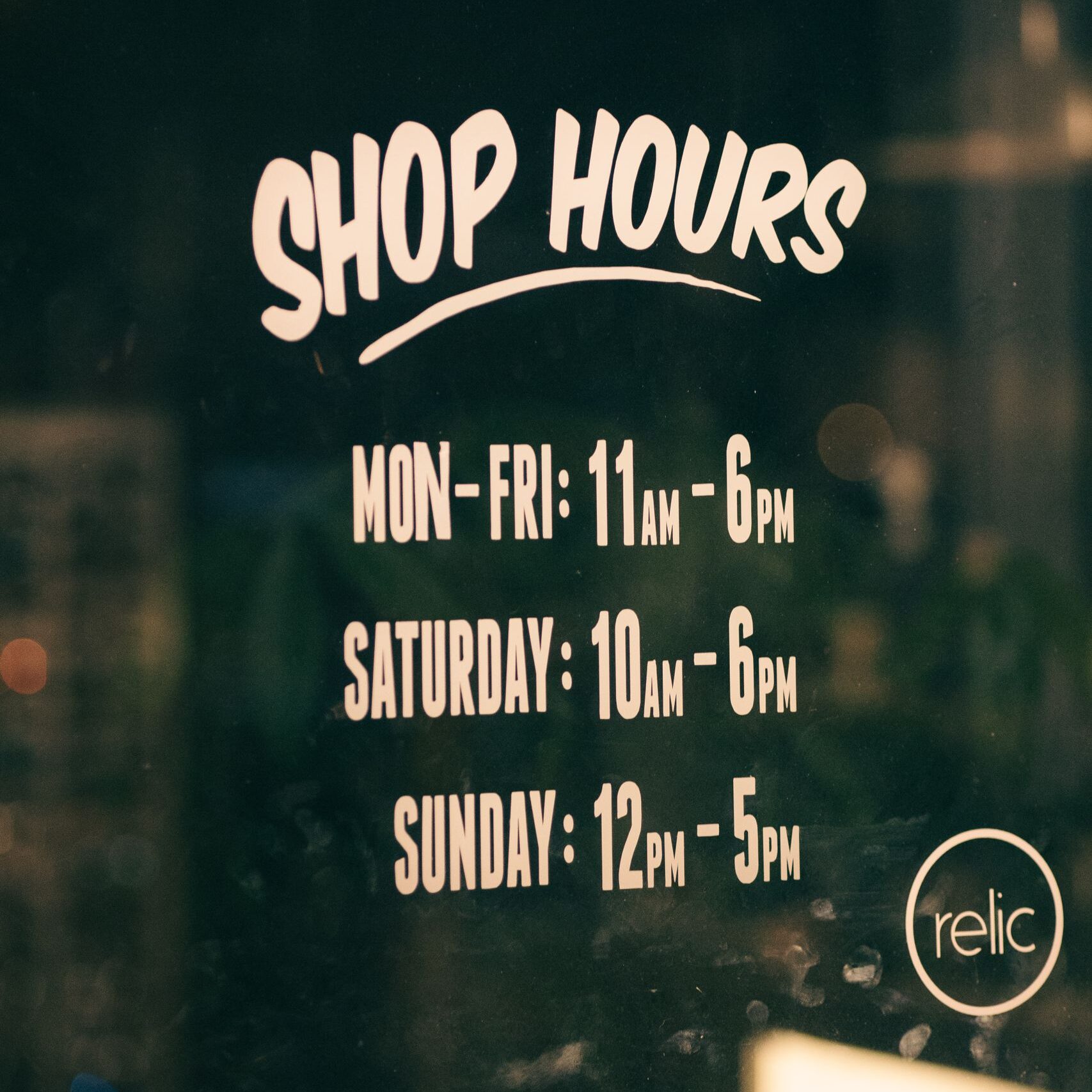 Close-up of store hours text on a glass panel with reflections.