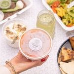 Hand holding Lebanese food container amidst an assortment of dishes, showcasing a vibrant meal setting.