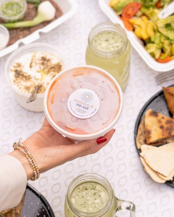 Photo by Alejandro Aznar Hand holding Lebanese food container amidst an assortment of dishes, showcasing a vibrant meal setting.